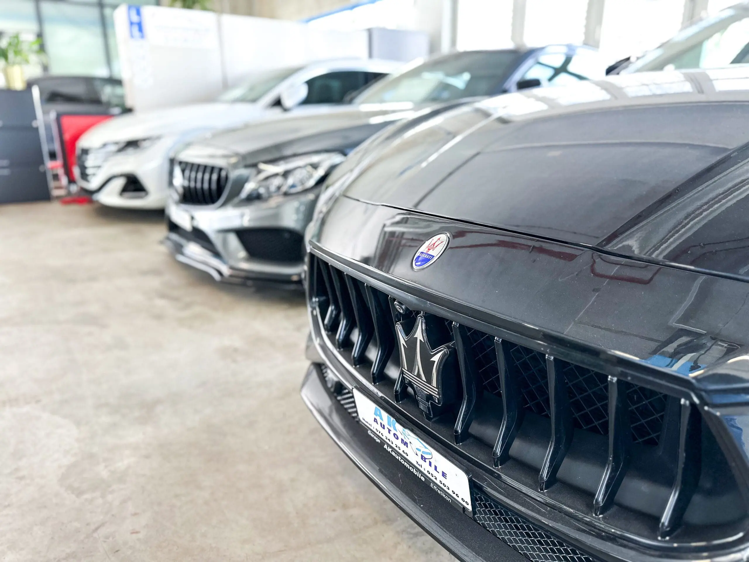 Detailansicht der Frontpartien luxuriöser Fahrzeuge im Showroom von AK Automobil GmbH mit Fokus auf die Kühlergrills.