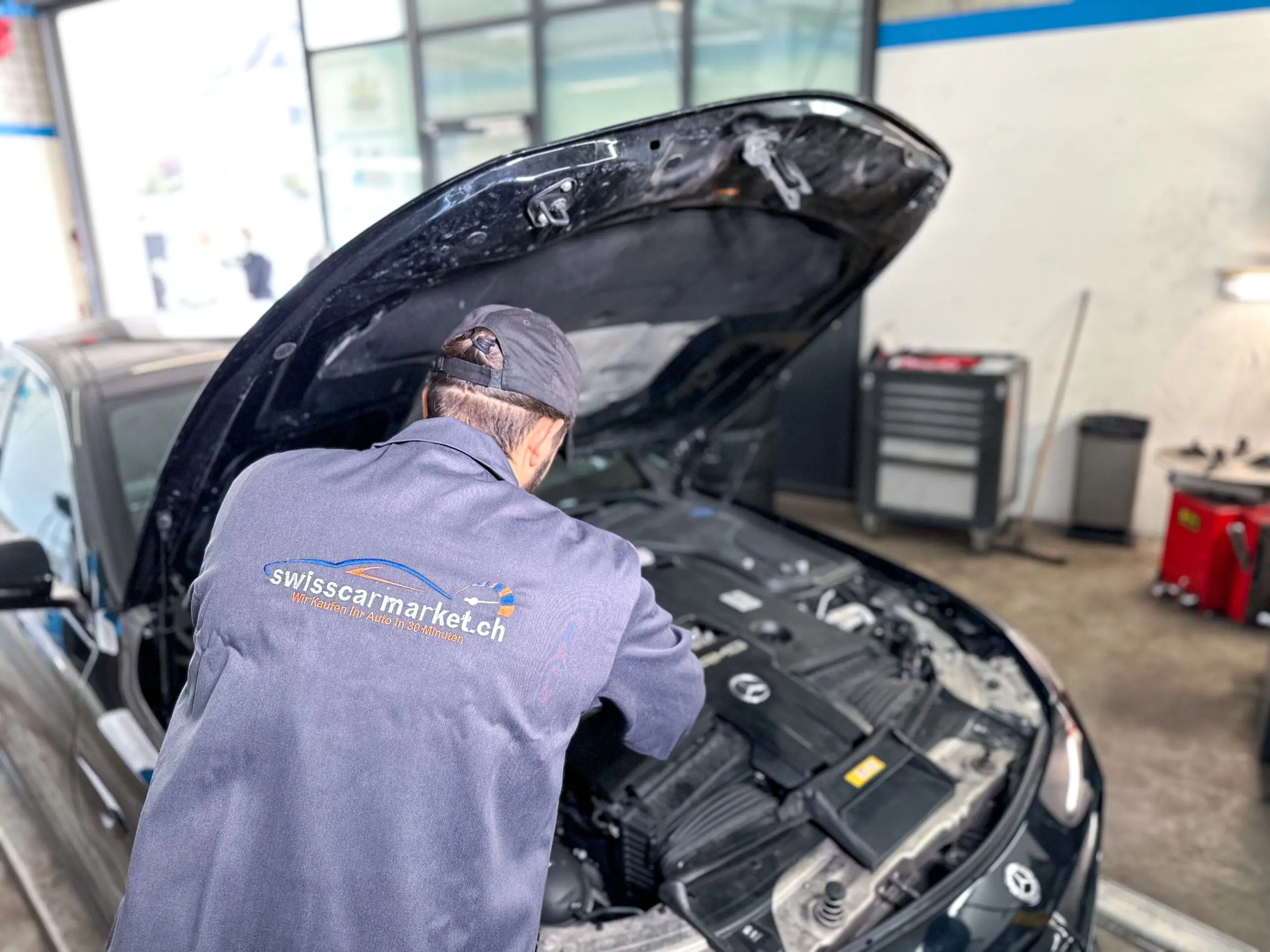 Ein Automechaniker in Arbeitskleidung untersucht den Motorraum eines Autos im Servicebereich eines Autohauses.
